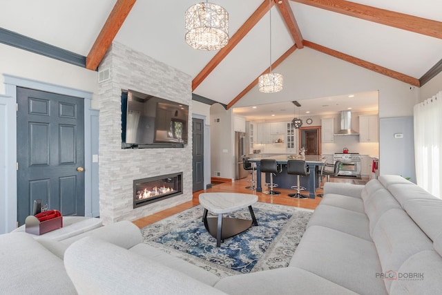 living room with high vaulted ceiling, beamed ceiling, light wood finished floors, a fireplace, and a chandelier