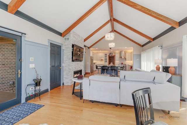 living area with beam ceiling, light wood-style floors, a large fireplace, and high vaulted ceiling