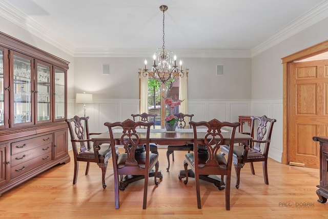 dining space featuring a decorative wall, a chandelier, a wainscoted wall, ornamental molding, and light wood finished floors