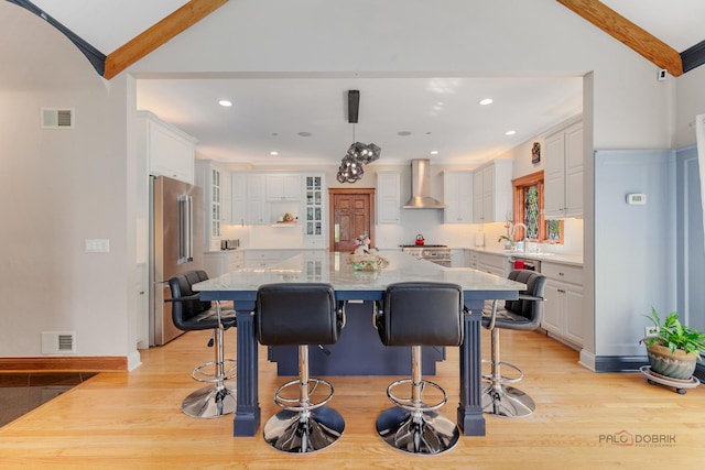 kitchen featuring wall chimney exhaust hood, stainless steel appliances, light wood-style flooring, white cabinetry, and a breakfast bar area