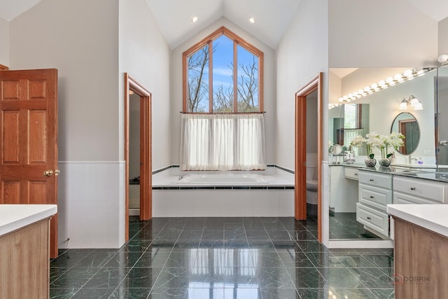 bathroom with high vaulted ceiling, granite floors, toilet, vanity, and a wainscoted wall