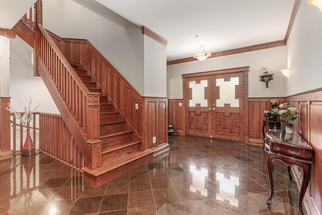 foyer entrance with wainscoting, granite tiled floors, ornamental molding, stairway, and a decorative wall