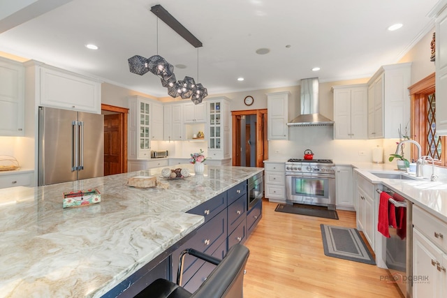 kitchen with premium appliances, wall chimney exhaust hood, white cabinetry, ornamental molding, and a sink