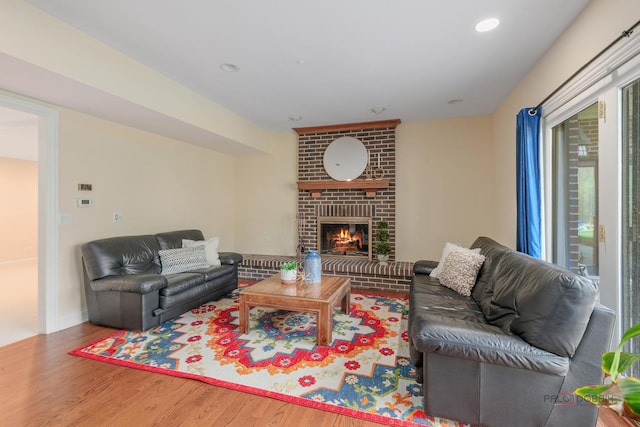 living area with wood finished floors, a brick fireplace, and recessed lighting