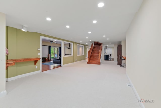 basement featuring stairs, light carpet, ceiling fan, baseboards, and recessed lighting
