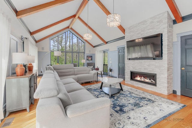 living area featuring beam ceiling, high vaulted ceiling, a fireplace, light wood-style flooring, and a chandelier