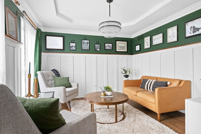 living area featuring an inviting chandelier, a decorative wall, wood finished floors, a tray ceiling, and ornamental molding