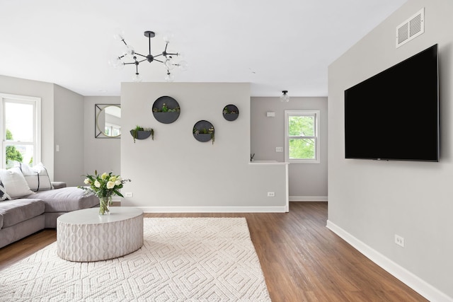 living room featuring a chandelier, baseboards, visible vents, and wood finished floors