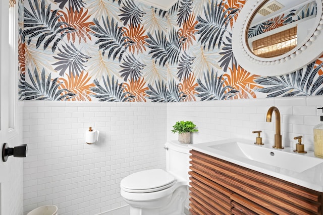 half bath featuring vanity, wallpapered walls, toilet, and tile walls