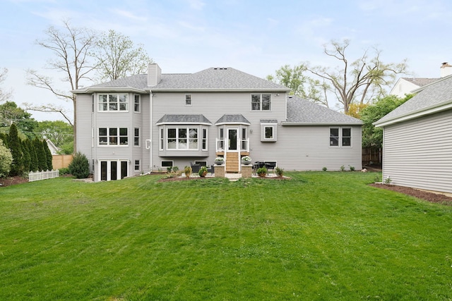 back of property with a shingled roof, fence, a yard, and a chimney