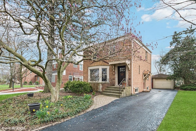 view of front of property featuring aphalt driveway, brick siding, an outdoor structure, and a detached garage