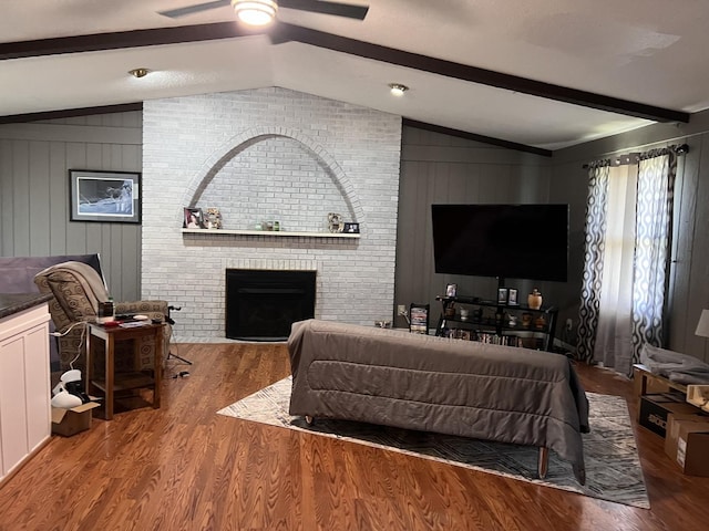 living area with a fireplace, vaulted ceiling with beams, a ceiling fan, and wood finished floors