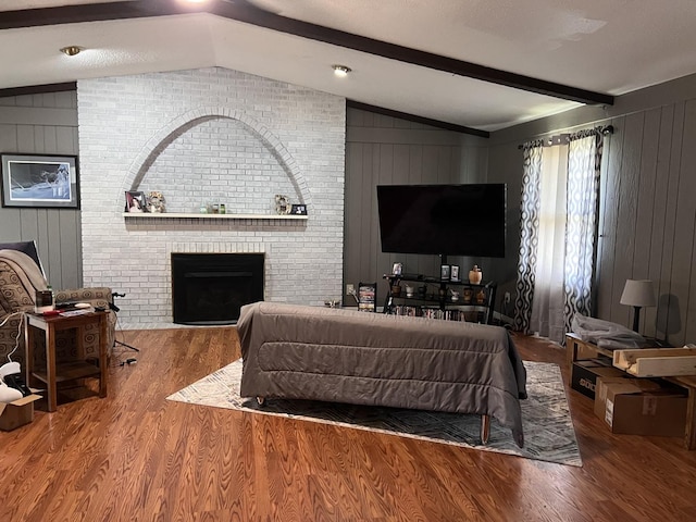 living area with wooden walls, a brick fireplace, wood finished floors, and lofted ceiling with beams