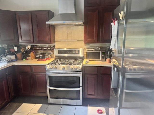 kitchen featuring appliances with stainless steel finishes, wall chimney exhaust hood, reddish brown cabinets, light countertops, and backsplash