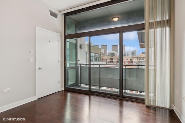 unfurnished room with baseboards, a city view, wood finished floors, and visible vents
