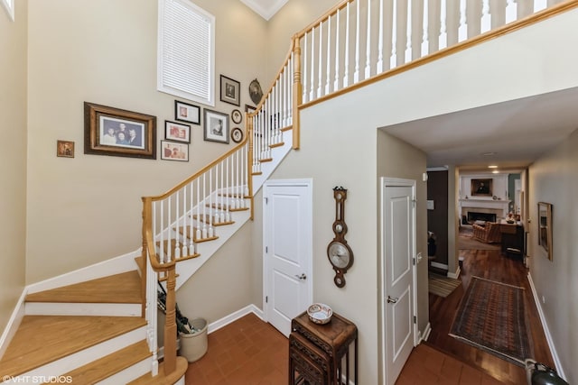stairway featuring baseboards, brick floor, a towering ceiling, and a fireplace