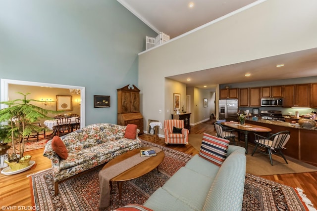 living area featuring crown molding, a high ceiling, recessed lighting, and light wood-style floors