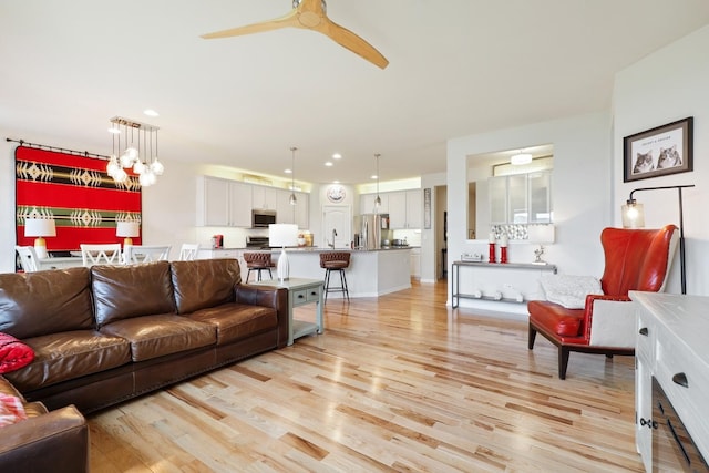 living room with light wood finished floors, recessed lighting, and ceiling fan with notable chandelier