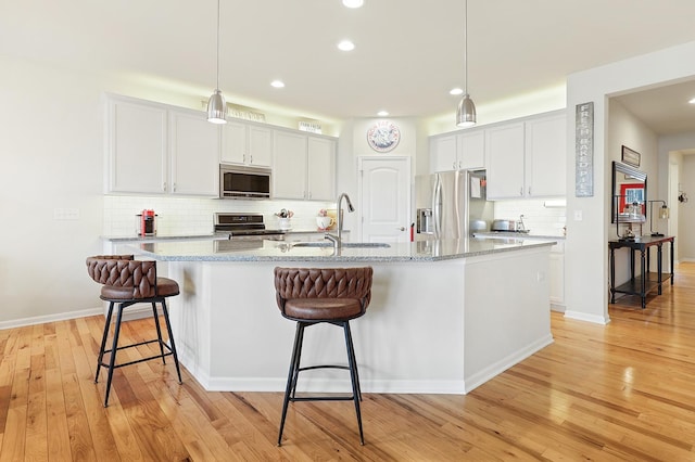 kitchen with light wood finished floors, stainless steel appliances, a sink, decorative backsplash, and a kitchen bar