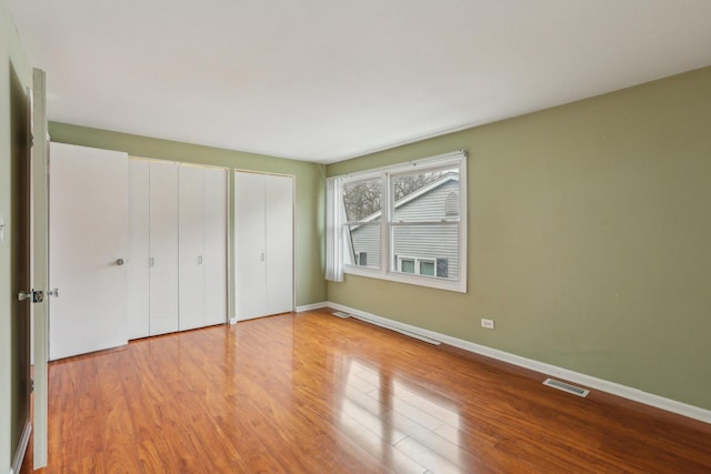 unfurnished bedroom with visible vents, baseboards, multiple closets, and wood finished floors