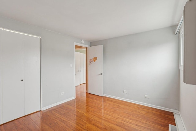 unfurnished bedroom with wood finished floors, baseboards, a closet, and visible vents