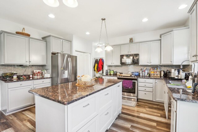 kitchen featuring a center island, tasteful backsplash, wood finished floors, a sink, and appliances with stainless steel finishes