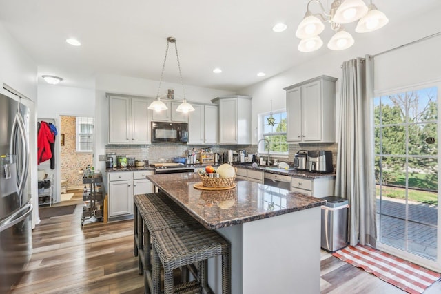 kitchen featuring wood finished floors, a sink, an inviting chandelier, stainless steel appliances, and backsplash