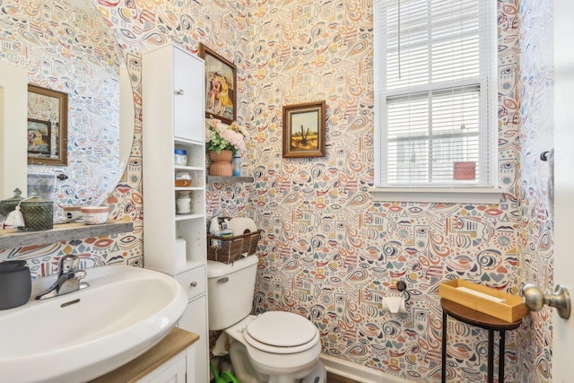half bathroom featuring toilet, a sink, and wallpapered walls