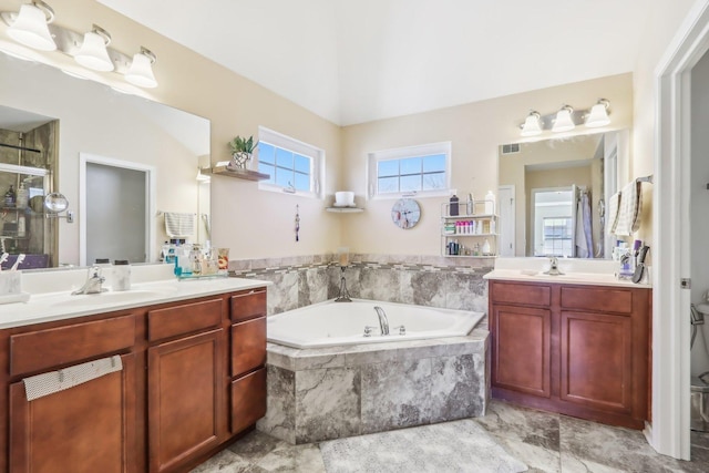 bathroom with two vanities, a bath, a stall shower, and a sink