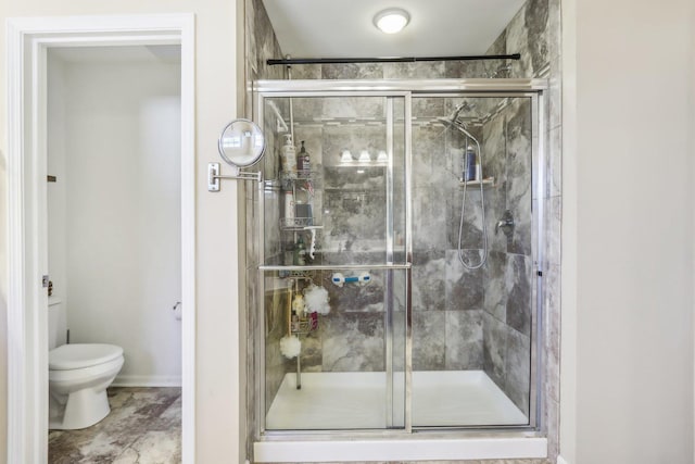 bathroom with baseboards, toilet, and a stall shower