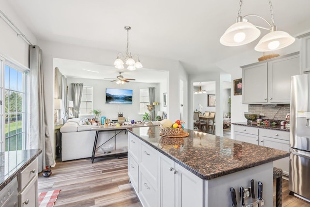 kitchen featuring hanging light fixtures, light wood-style flooring, tasteful backsplash, appliances with stainless steel finishes, and ceiling fan with notable chandelier