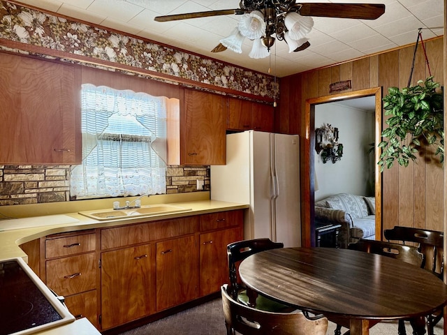 kitchen with ceiling fan, freestanding refrigerator, brown cabinetry, light countertops, and a sink