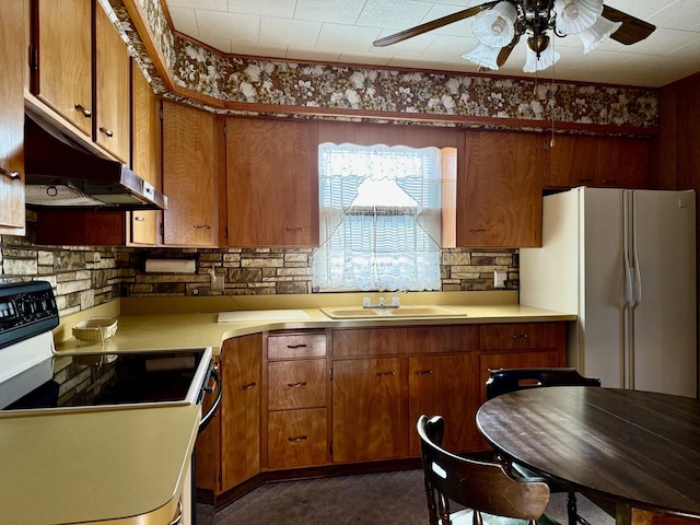 kitchen featuring freestanding refrigerator, a ceiling fan, under cabinet range hood, range with electric cooktop, and a sink