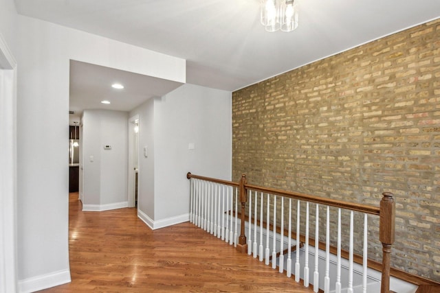 corridor with brick wall, an upstairs landing, baseboards, and wood finished floors