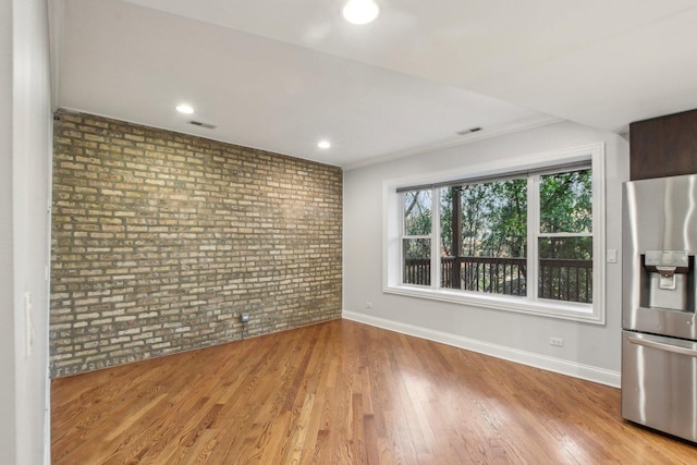 interior space featuring brick wall, wood finished floors, baseboards, and visible vents