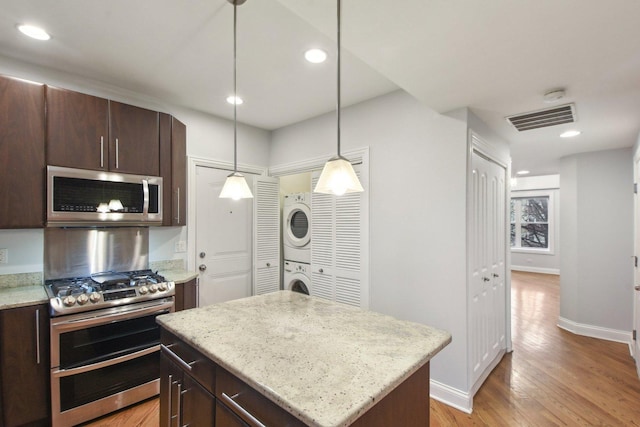 kitchen featuring visible vents, appliances with stainless steel finishes, dark brown cabinetry, and stacked washer and clothes dryer