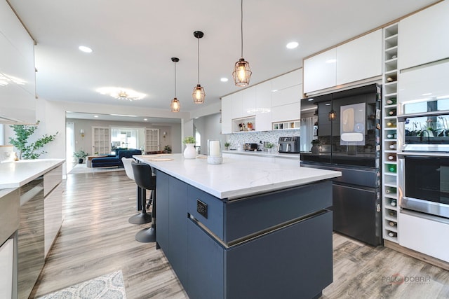 kitchen featuring oven, white cabinets, light wood-type flooring, a center island, and open floor plan