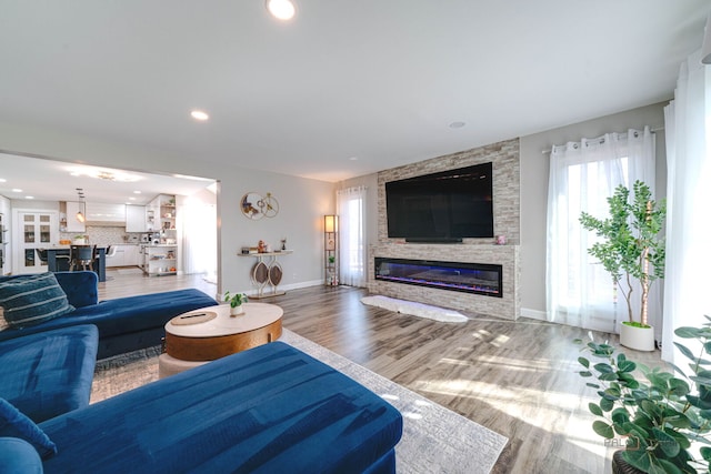 living area with baseboards, recessed lighting, wood finished floors, and a stone fireplace