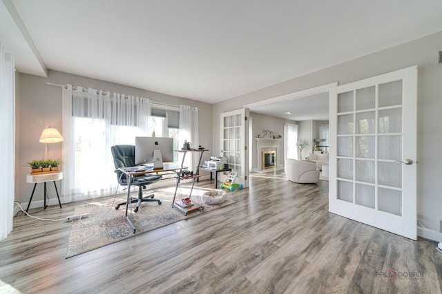living area with a glass covered fireplace, wood finished floors, french doors, and baseboards