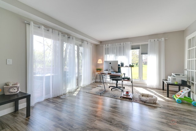 office with visible vents, baseboards, wood finished floors, and a healthy amount of sunlight