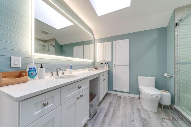 full bath featuring a sink, a shower stall, toilet, double vanity, and a skylight