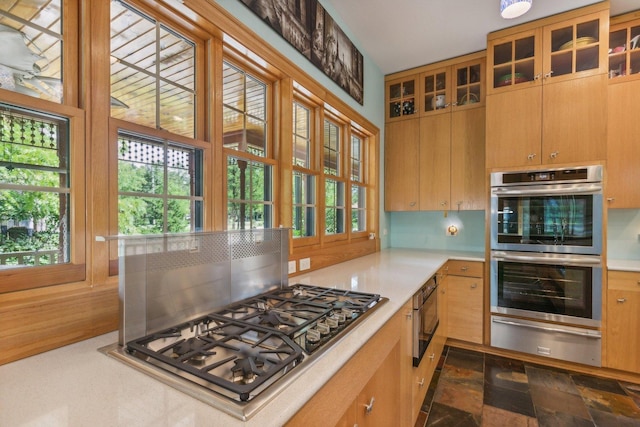 kitchen with light countertops, a warming drawer, appliances with stainless steel finishes, and glass insert cabinets