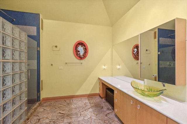 bathroom featuring a tile shower, vanity, baseboards, and lofted ceiling
