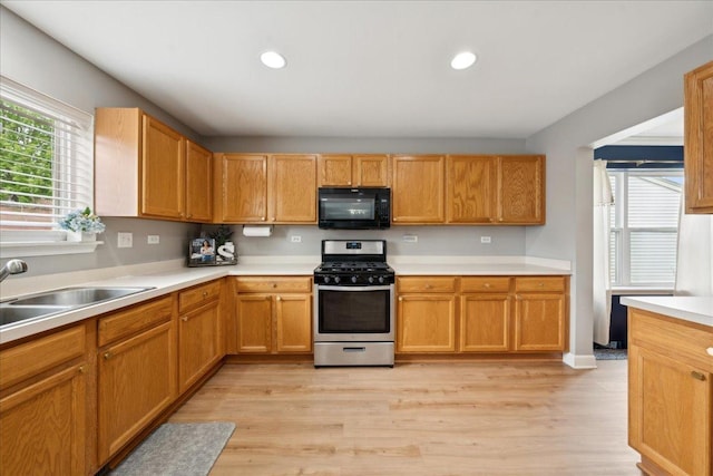 kitchen with black microwave, light wood-type flooring, gas stove, a sink, and light countertops