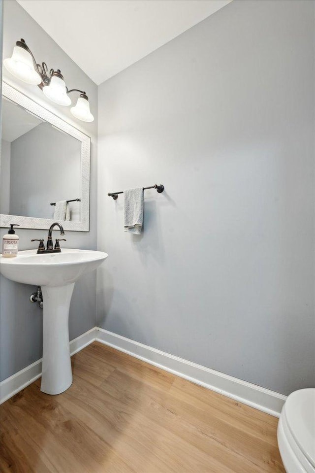 half bathroom with toilet, baseboards, a sink, and wood finished floors