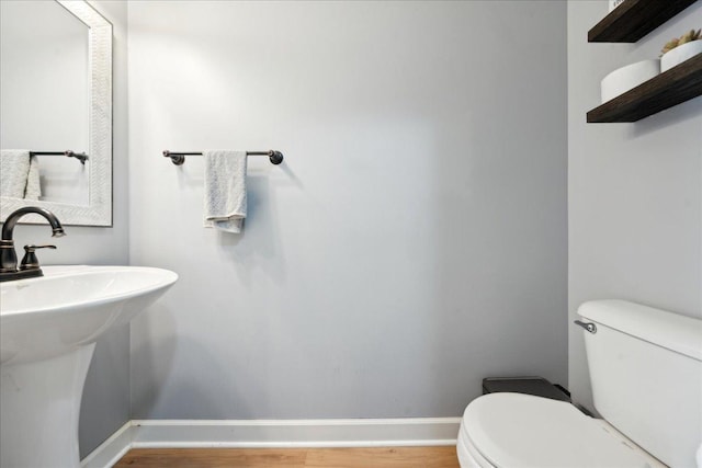 half bathroom with a sink, baseboards, toilet, and wood finished floors