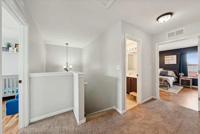 corridor with baseboards, visible vents, light carpet, and an upstairs landing