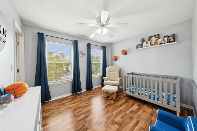 bedroom featuring baseboards, a ceiling fan, a crib, and wood finished floors