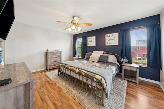 bedroom featuring baseboards, ceiling fan, multiple windows, and wood finished floors