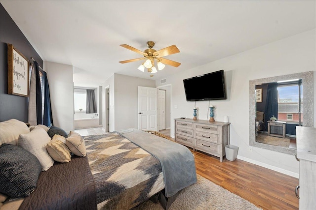 bedroom with ceiling fan, visible vents, wood finished floors, baseboards, and connected bathroom